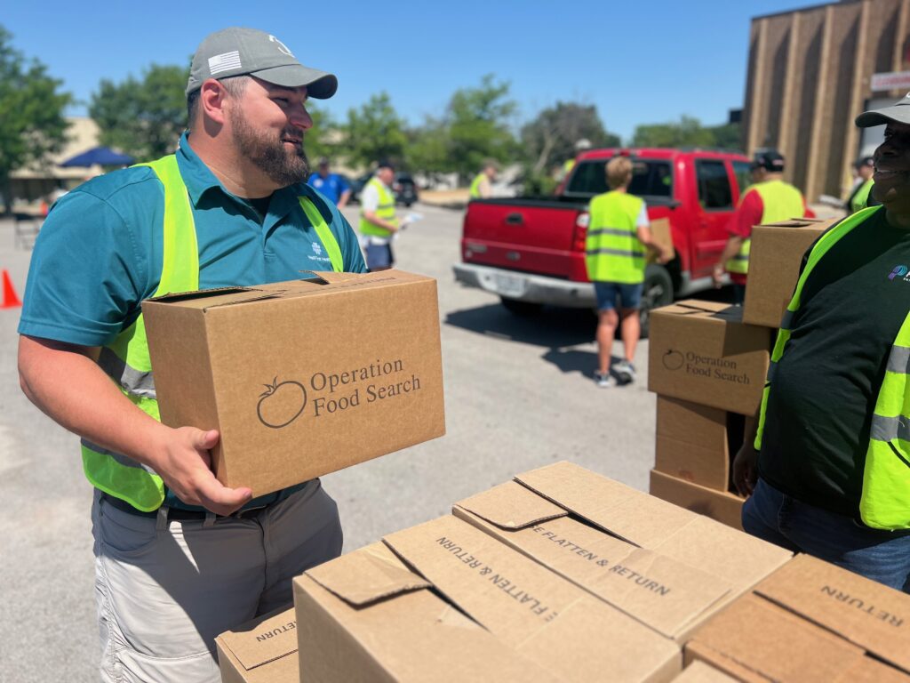 Volunteers distribute box of food from Operation Food Search to the community in drive-thru event.