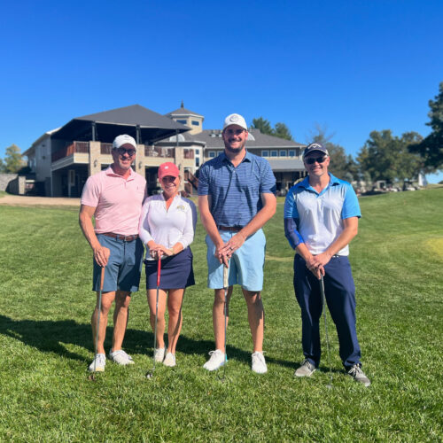 Three men and a woman stand on the golf course.