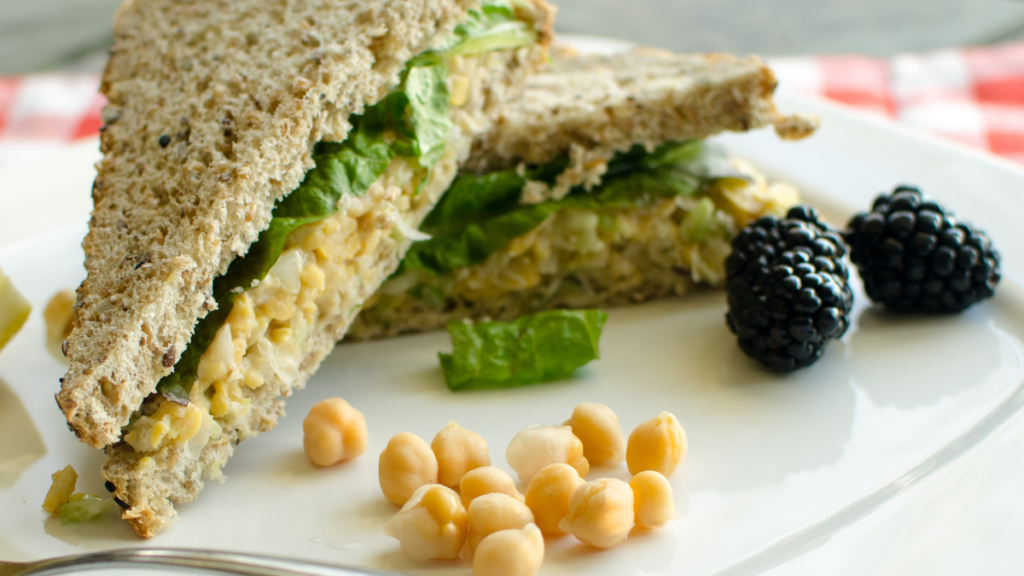 halved chickpea salad sandwich plated with chickpeas and berries
