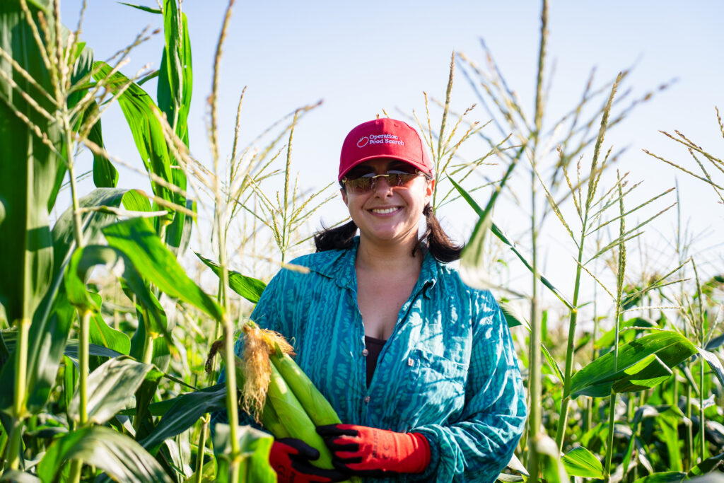 Gleaning Volunteer Smiling and Holding Gleaned Produce in Cornfield